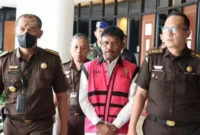 Keterangan Foto : Jhonny plate Menkominfo usai diperiksa mengenakan rompi khas Kejagung dan tangan terborgol.